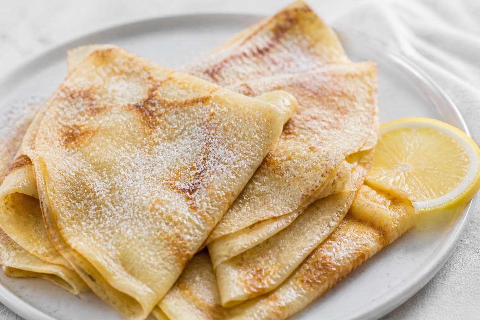 Thin gluten-free sourdough crepes folded on a plate with lemon and maple